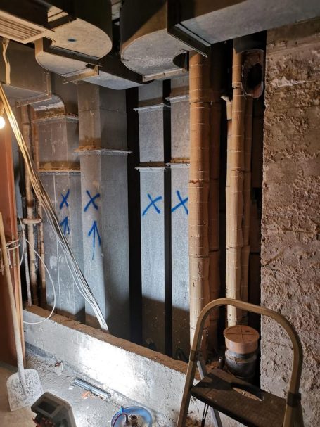 Demontage Lüftungskanäle Baustelle mit Wänden und Rohren, gekennzeichnet mit blauen X.