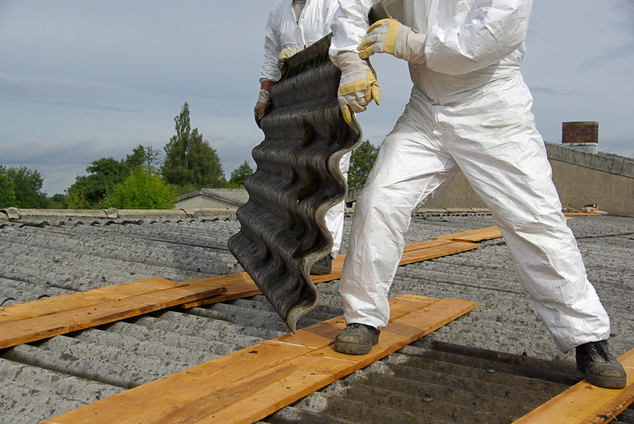 Eternit Dachplatten (Berliner Welle) Zwei Arbeiter in Schutzkleidung verlegen Wellblech auf einem Dach.